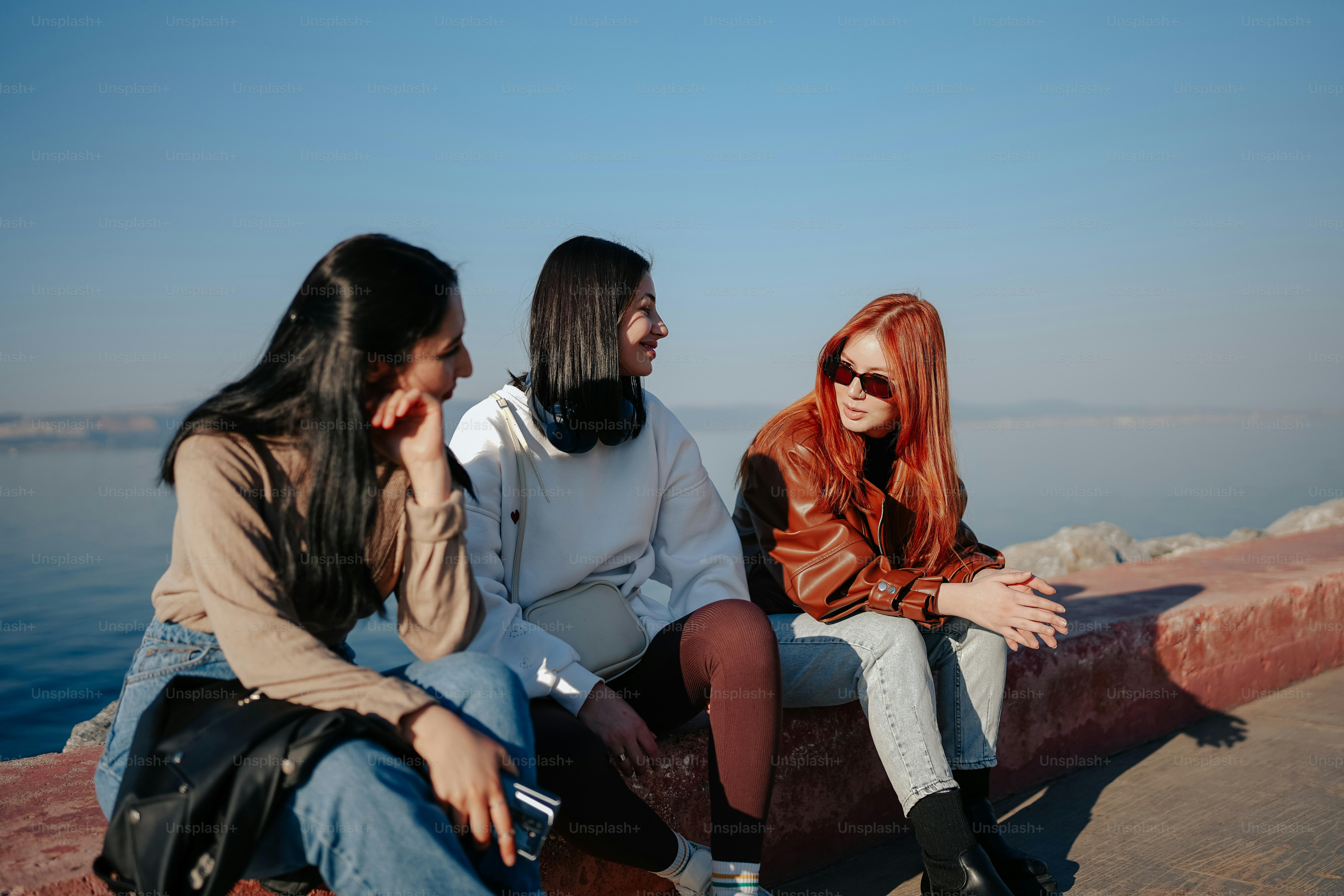 three young women sitting on a wall near the water