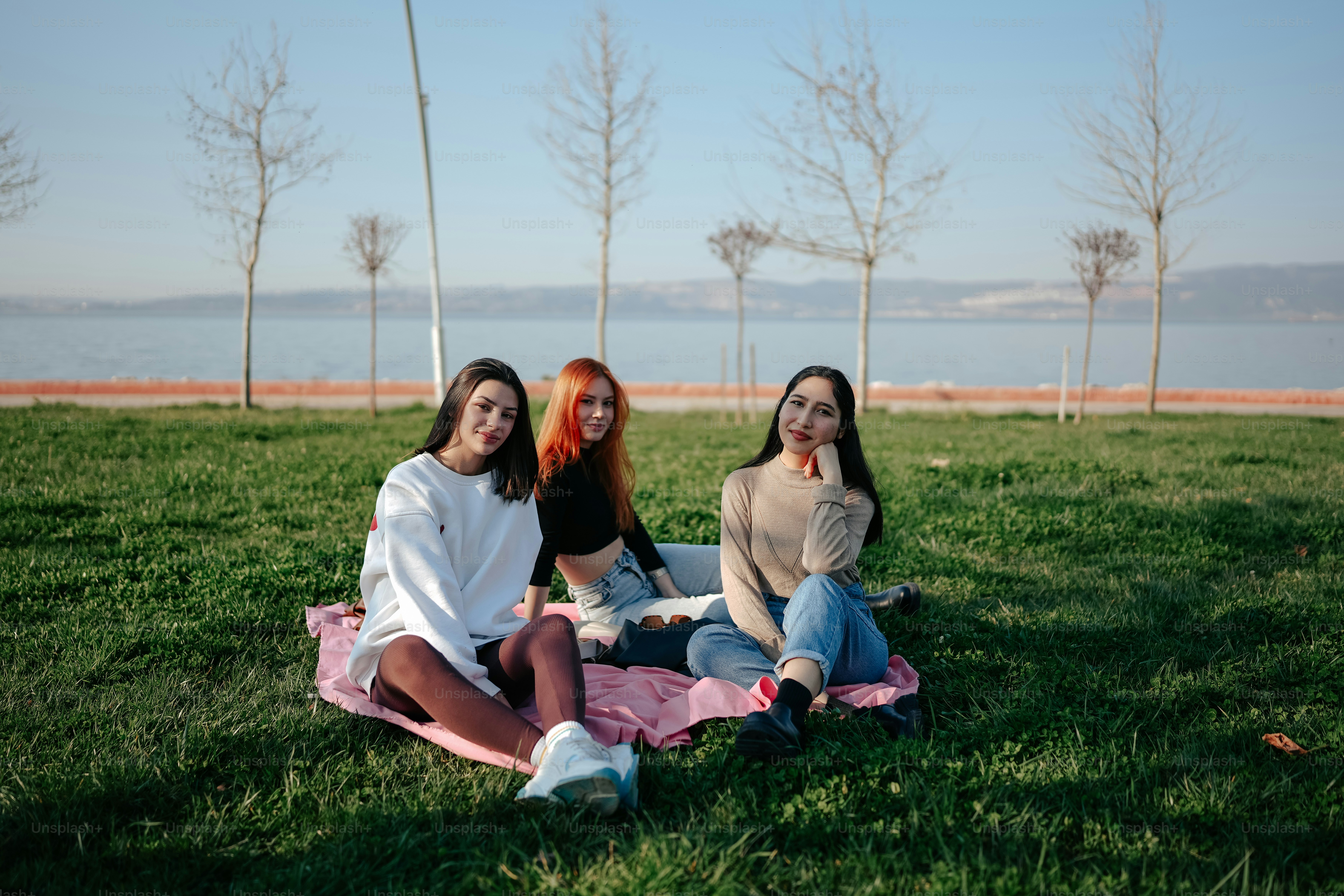 three women sitting on a blanket in a park