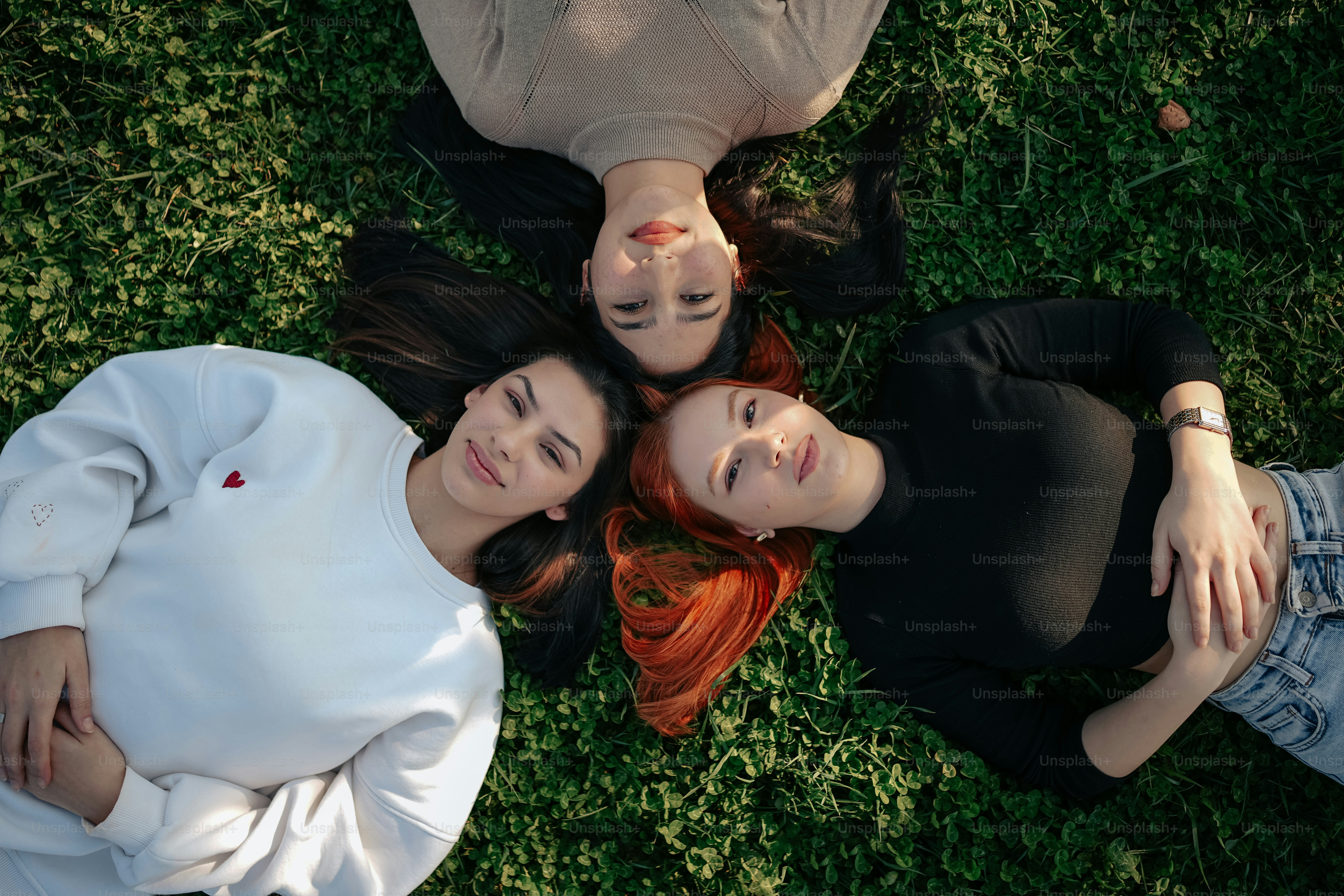 three young women laying on the grass with their arms around each other