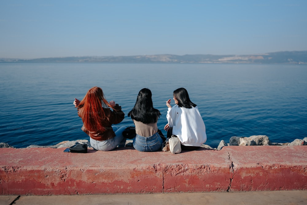 three women sitting on a ledge looking out at the water
