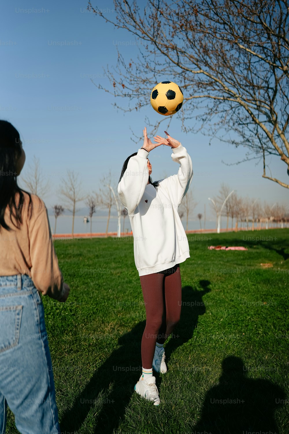 흰색 재킷을 입은 여성이 노란색 축구공을 들고 있다