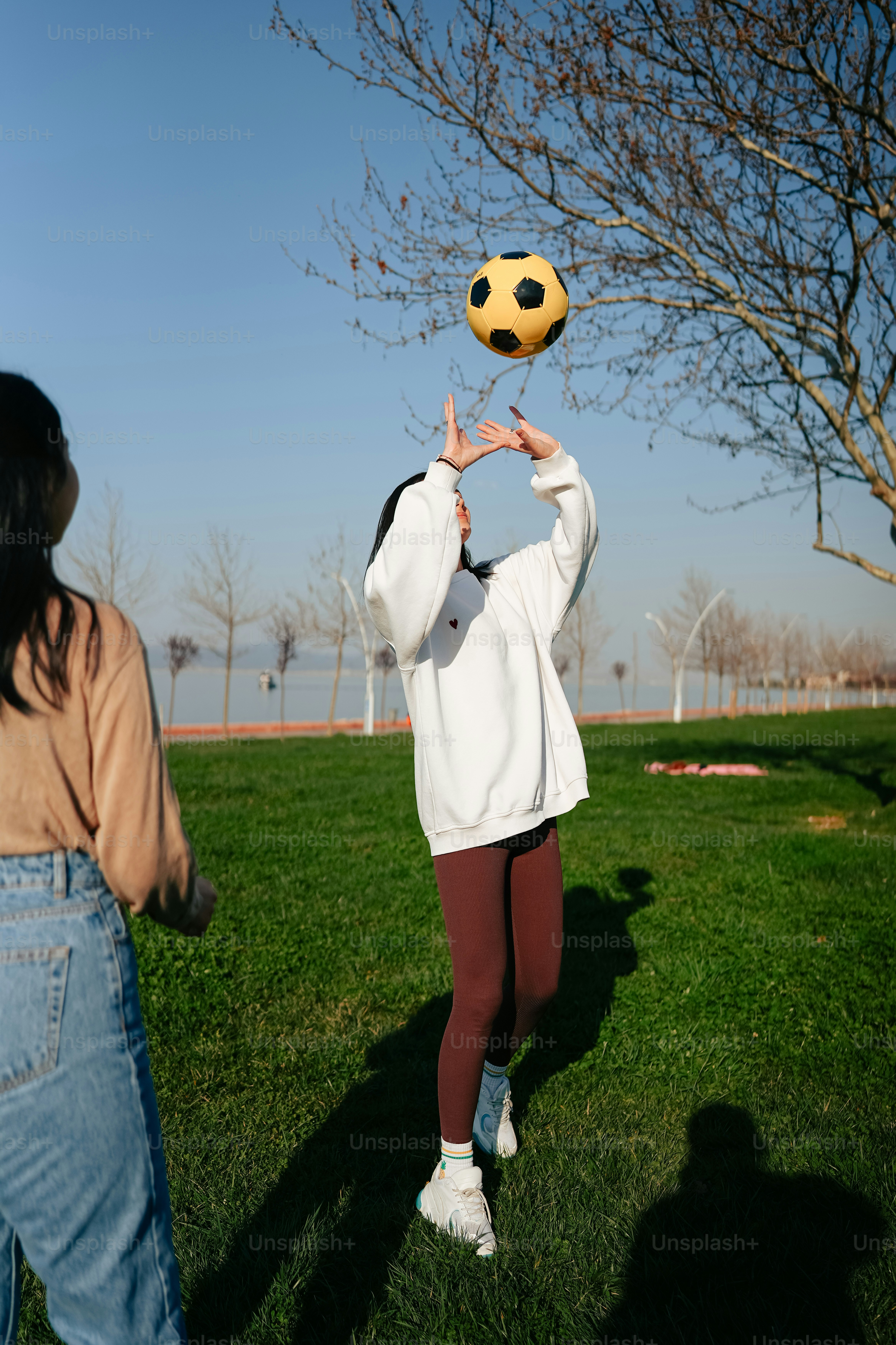 a woman in a white jacket is holding a yellow soccer ball