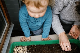 a woman and a child are looking at a tray of dirt