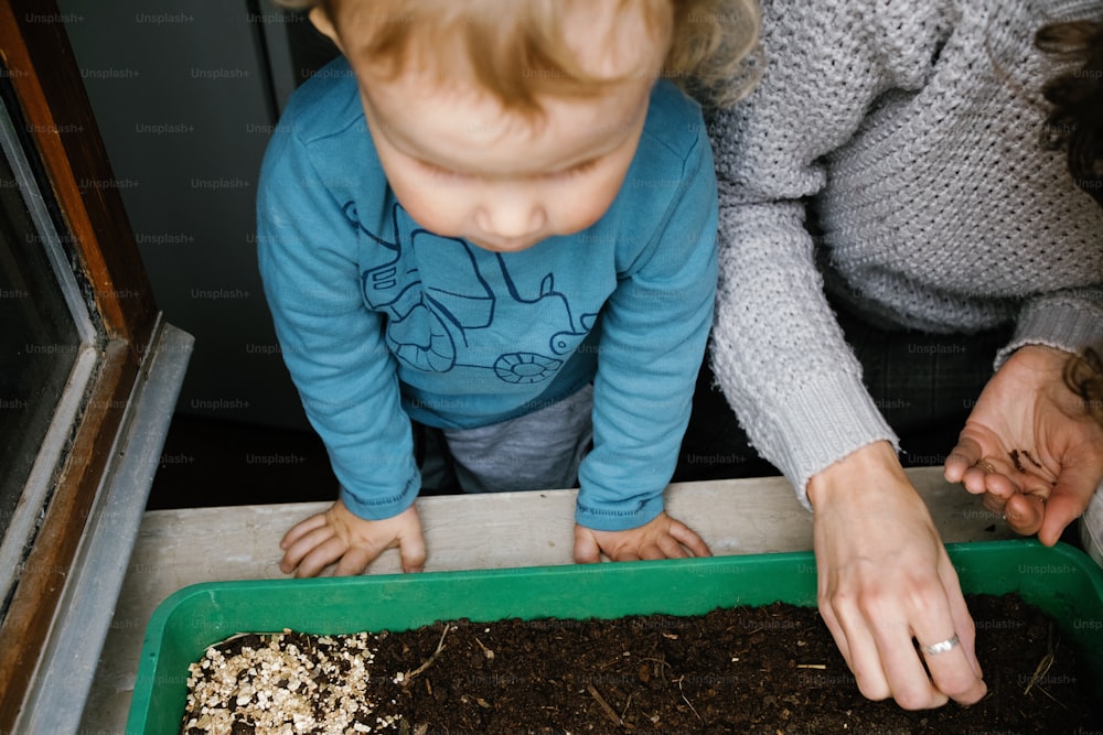 a woman and a child are looking at a tray of dirt