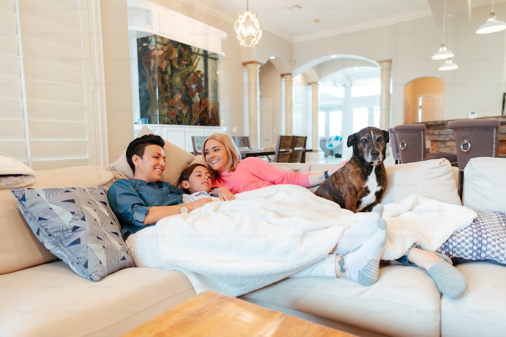 um homem, mulher e criança deitados em um sofá com um cão
