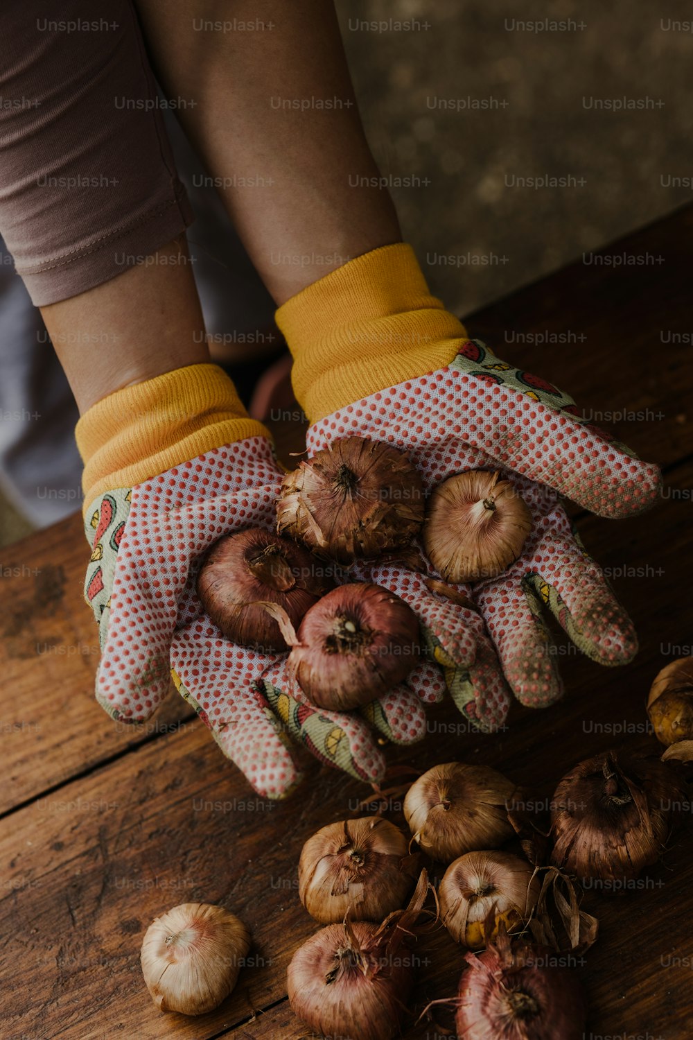 a person wearing gloves and holding a bunch of onions