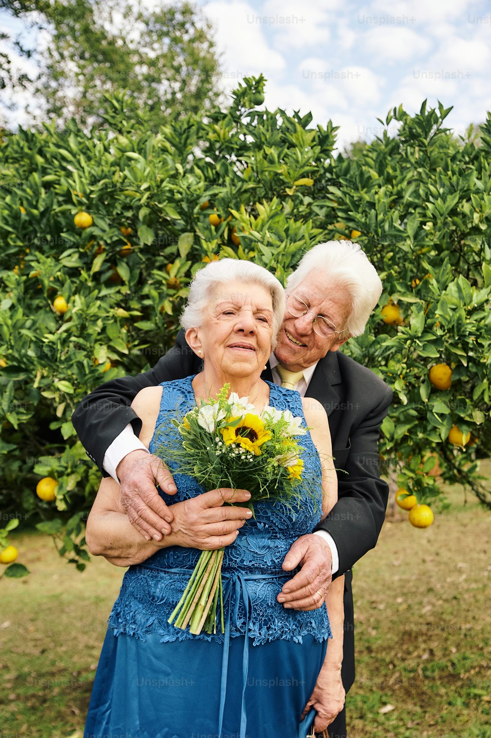 an older couple embracing each other in front of an orange tree