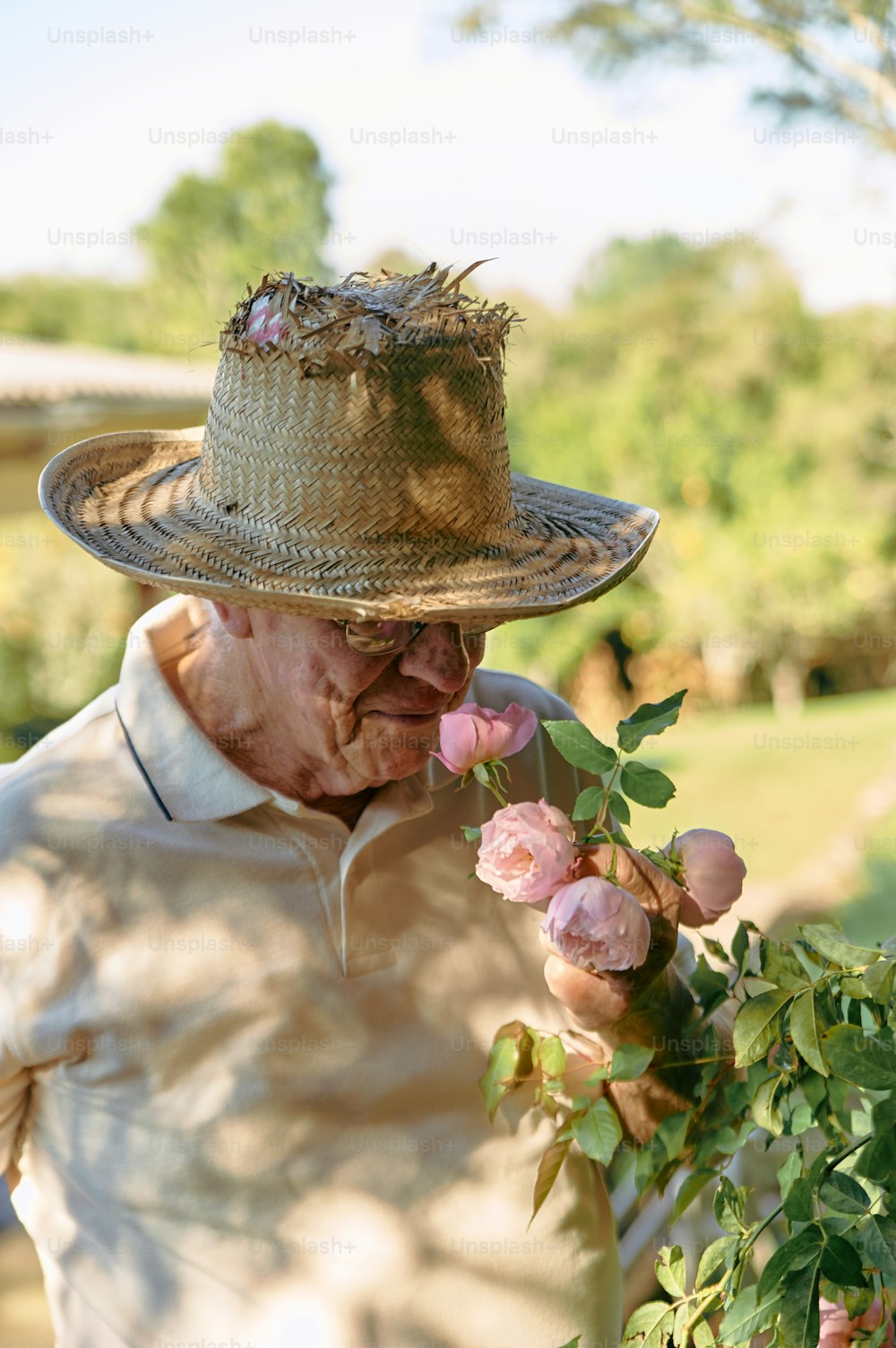 an old man wearing a straw hat smelling a flower