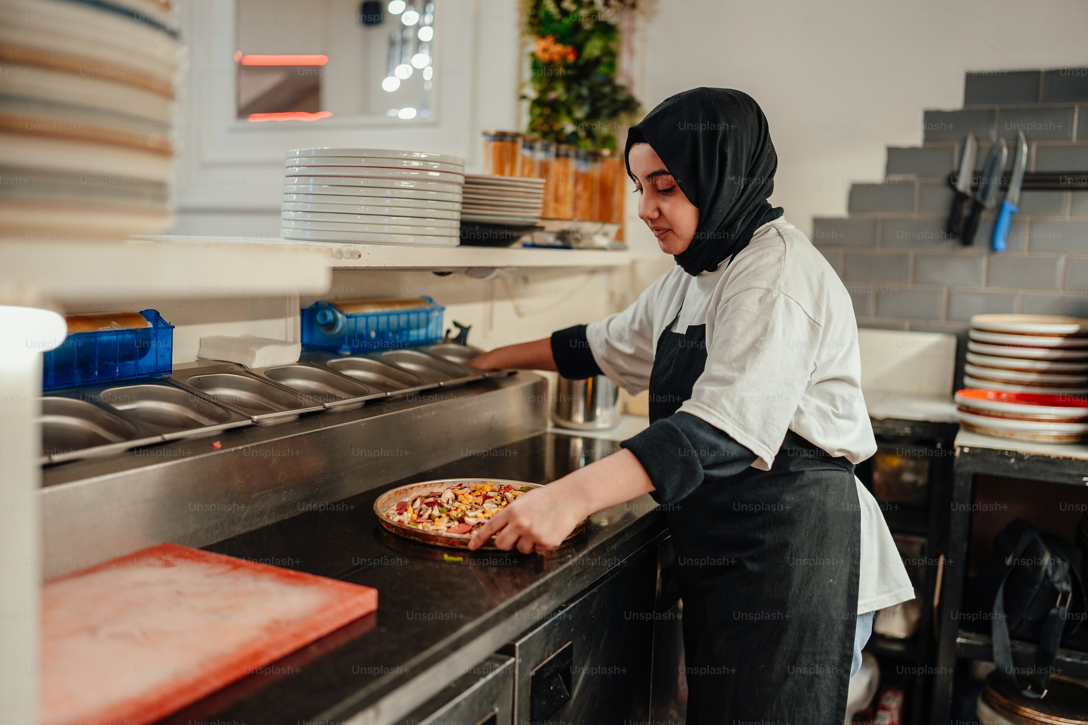 a woman in a hijab putting a pizza into the oven