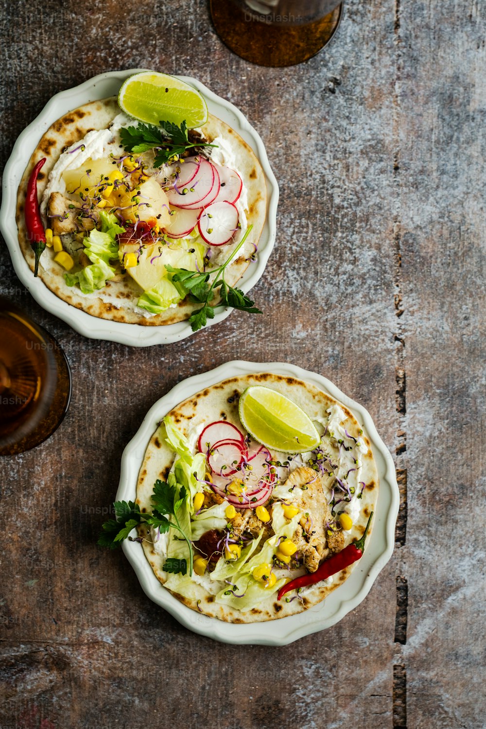 two burritos with toppings sit on a table next to a glass of