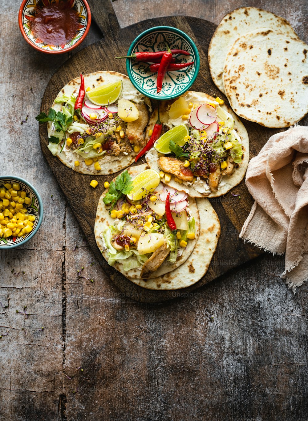 a wooden cutting board topped with tacos and corn