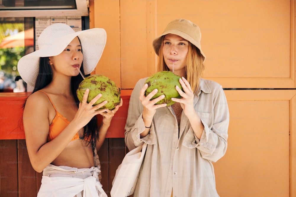two beautiful women standing next to each other holding green fruit