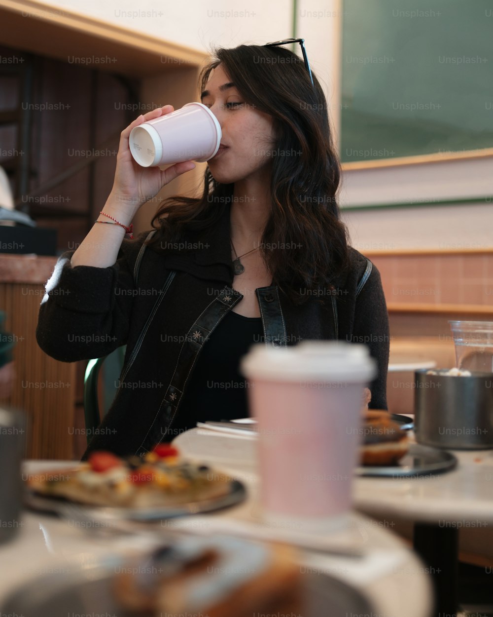 a woman sitting at a table drinking from a cup