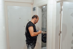 a man in a black shirt is painting a white door