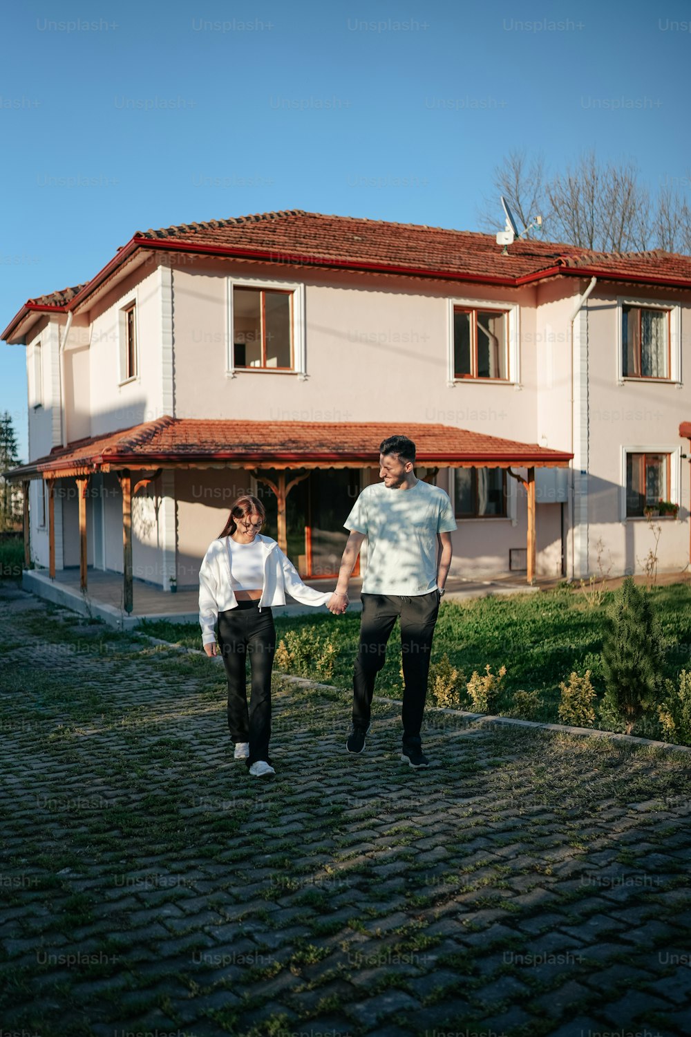 um homem e uma mulher de mãos dadas na frente de uma casa