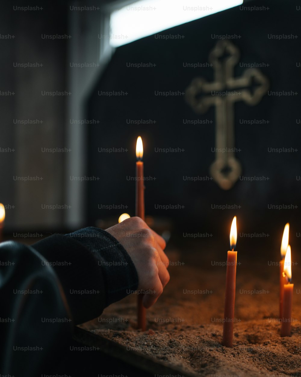 a person holding a lit candle in front of a cross