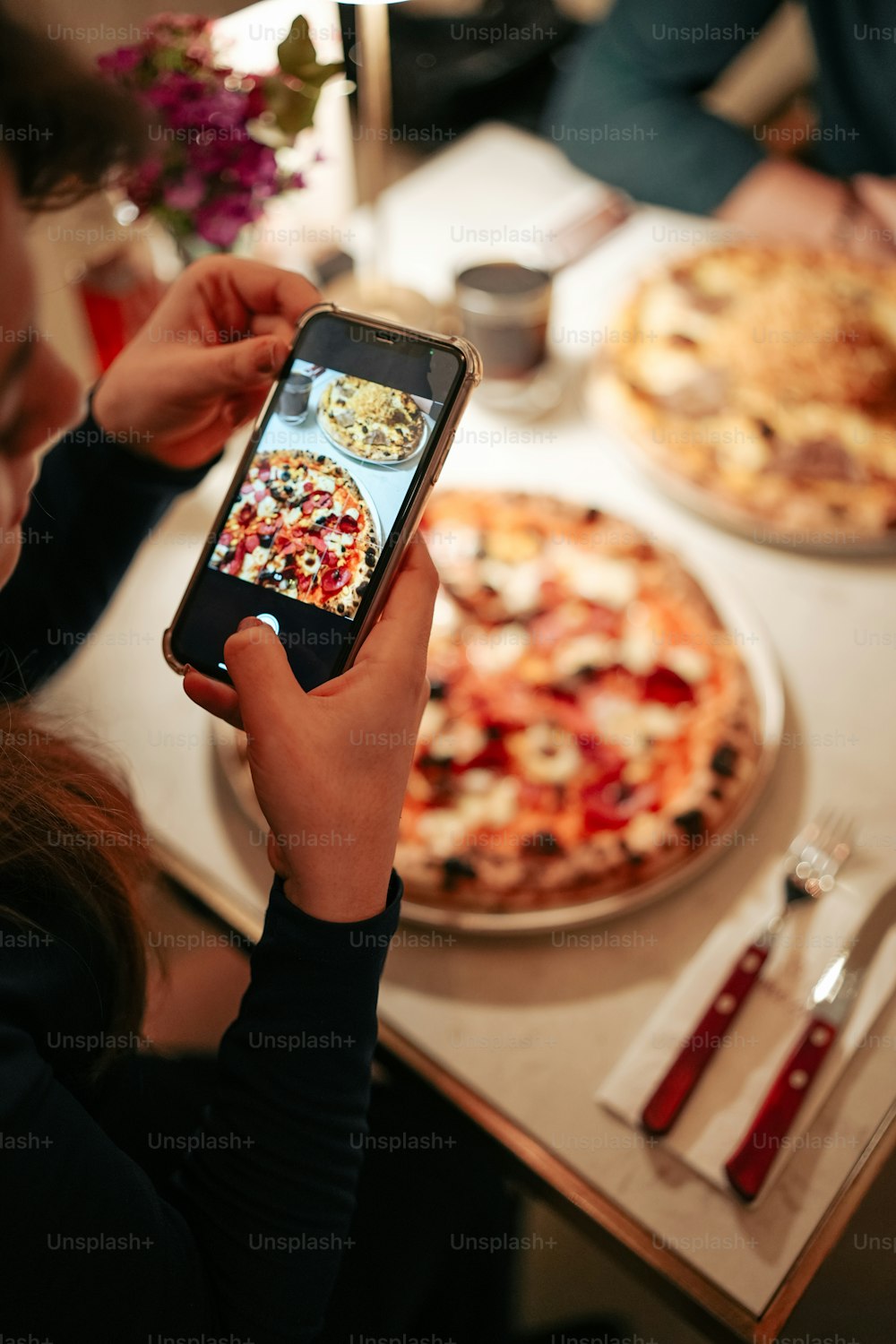 a woman taking a picture of a pizza with her phone