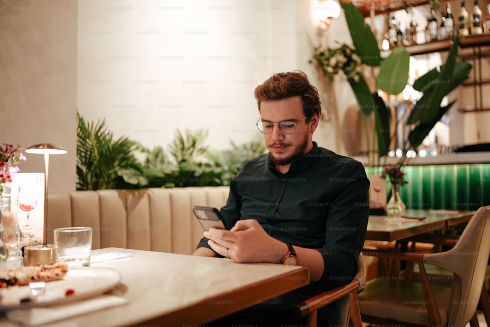 um homem sentado em uma mesa olhando para um telefone celular