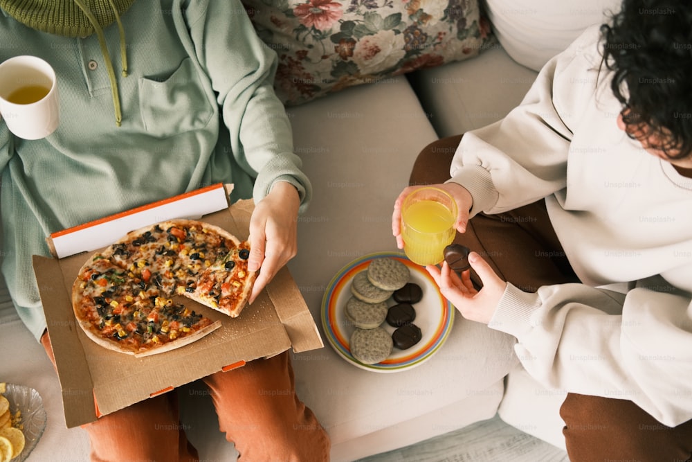 um casal de pessoas sentadas em um sofá comendo pizza