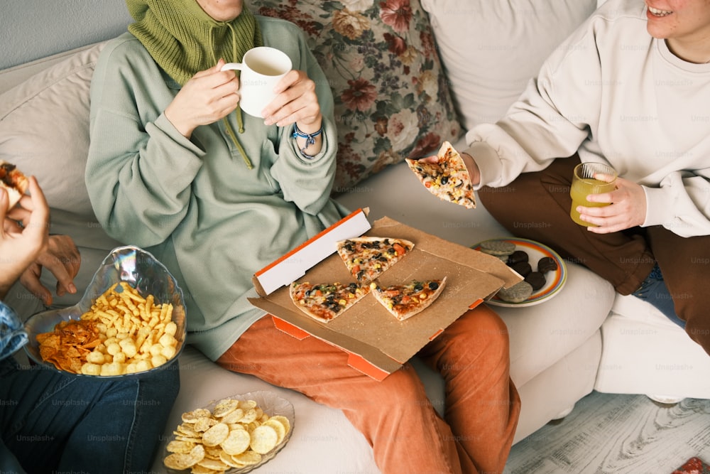 um grupo de pessoas sentadas em um sofá comendo pizza
