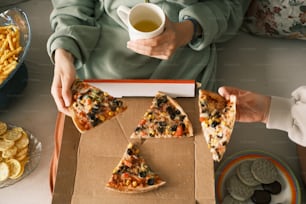 a person holding a box of pizza and a cup of tea