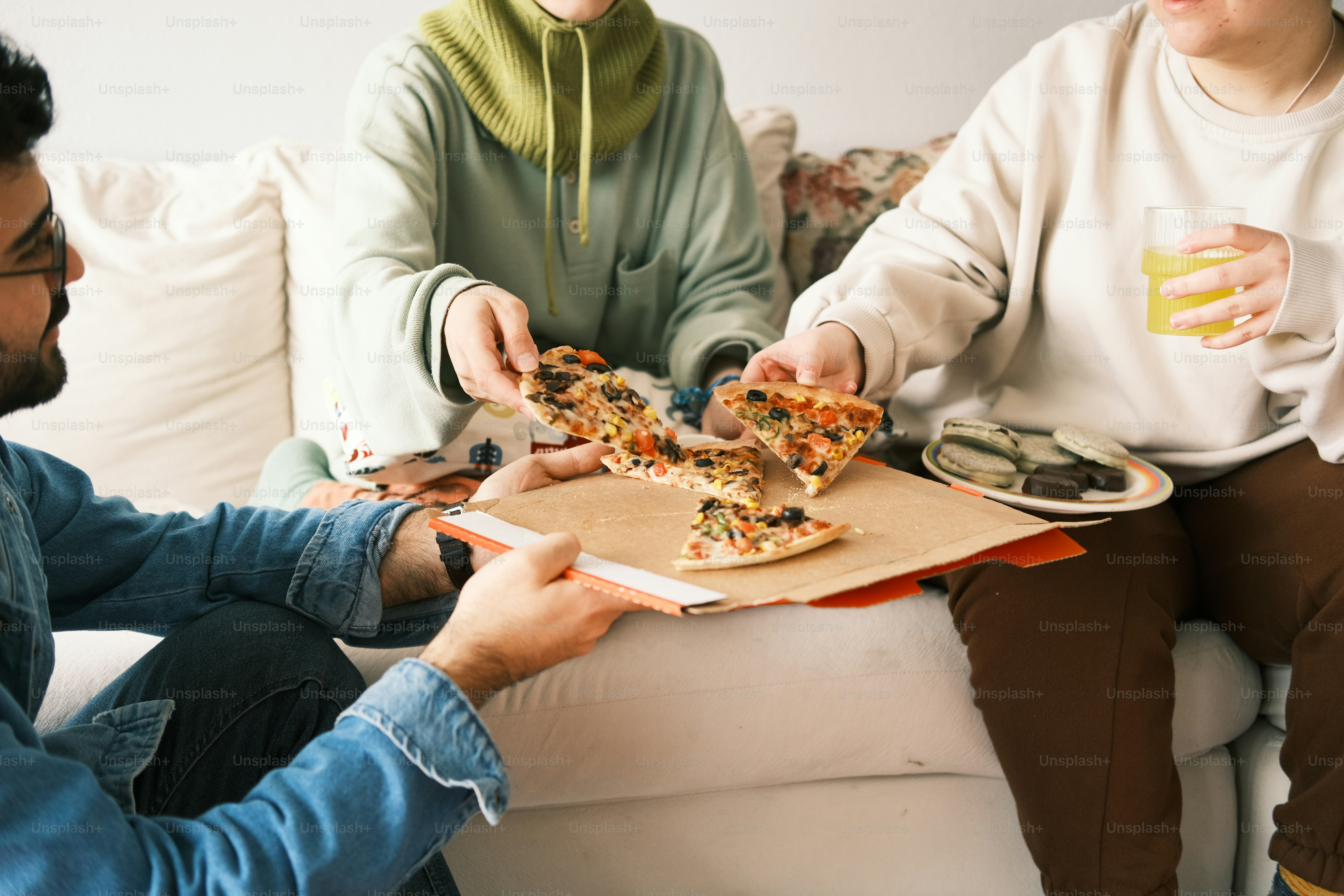 a group of people sitting on a couch eating pizza