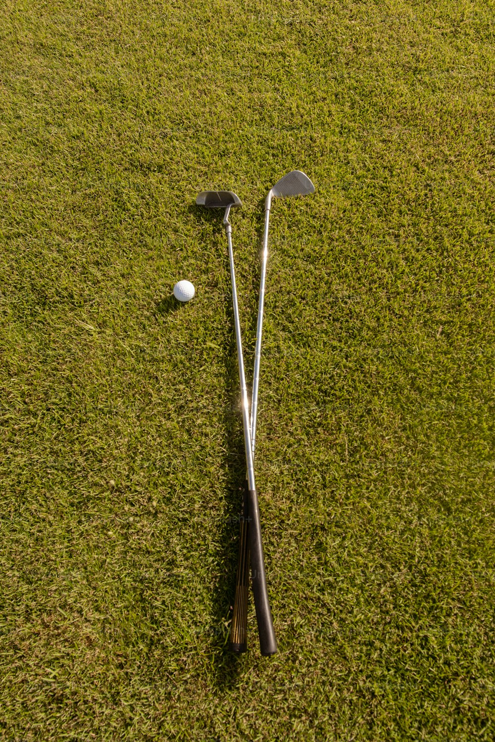 two golf clubs and a ball laying on the grass