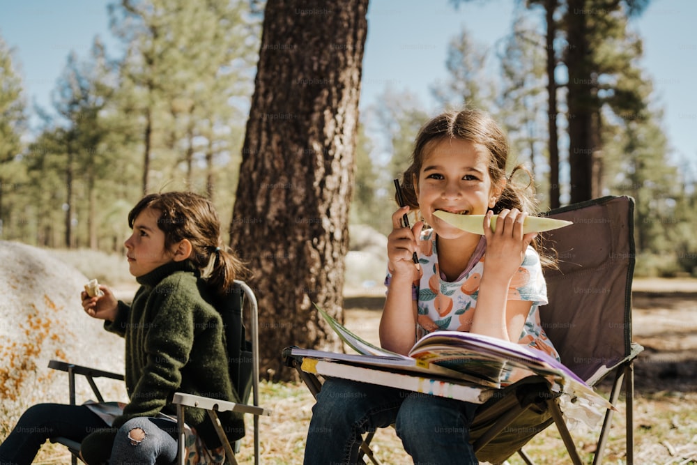 two young girls sitting in folding chairs in the woods