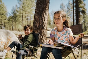 two young children sitting in folding chairs in the woods