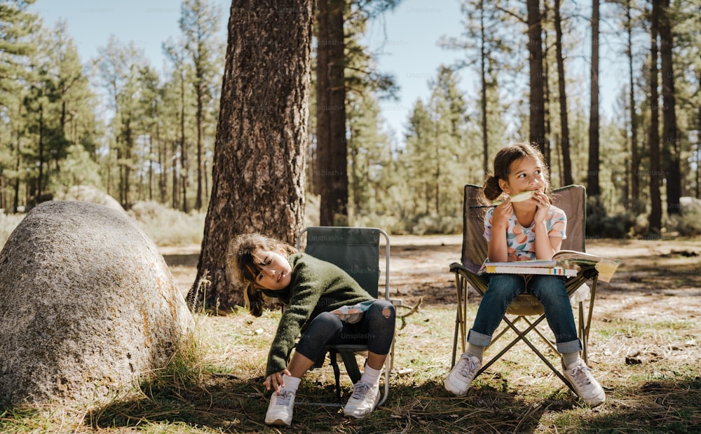 a couple of kids sitting in chairs in the woods