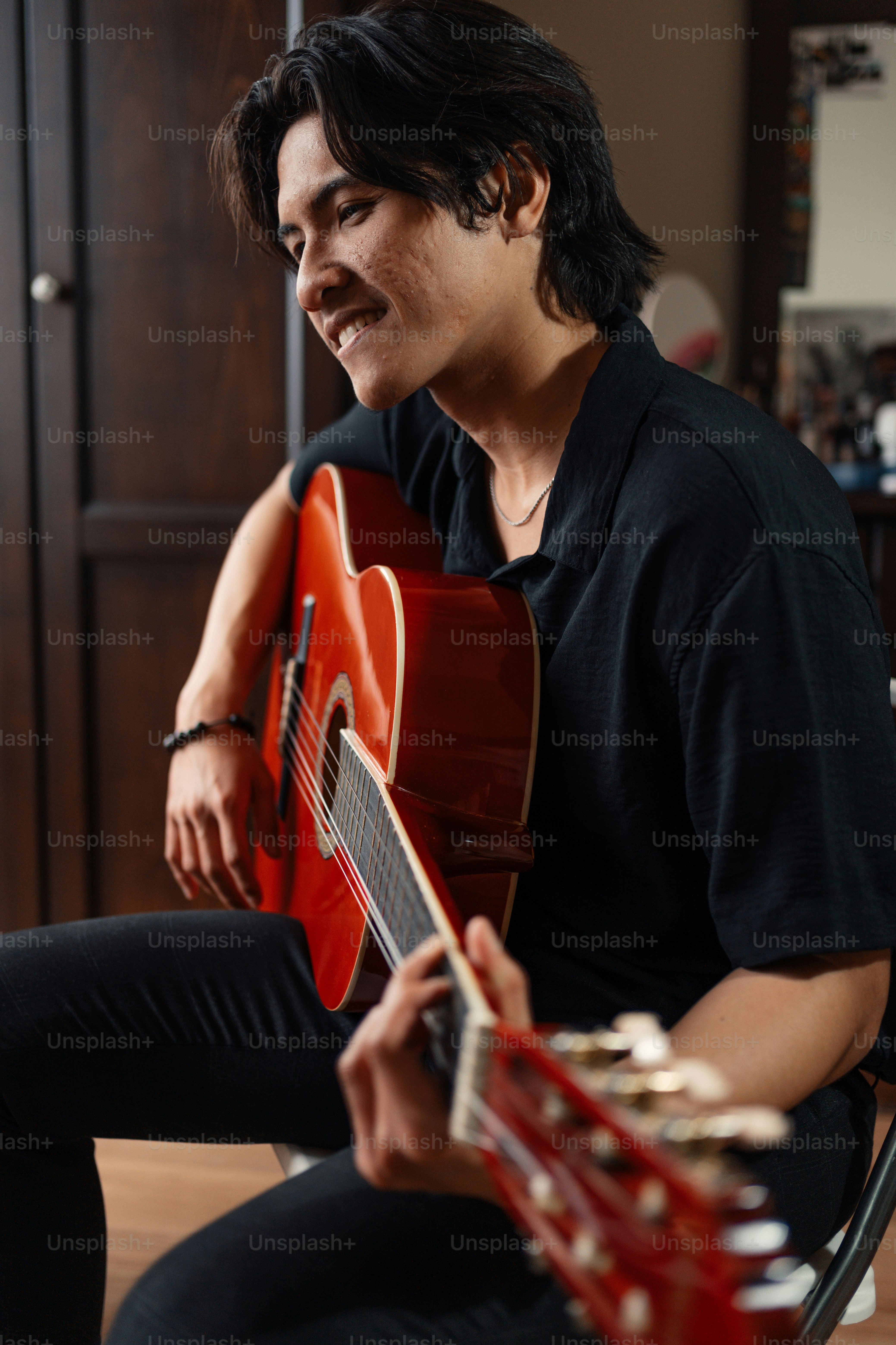 A man sitting on a chair holding a red guitar photo – Playing guitar ...