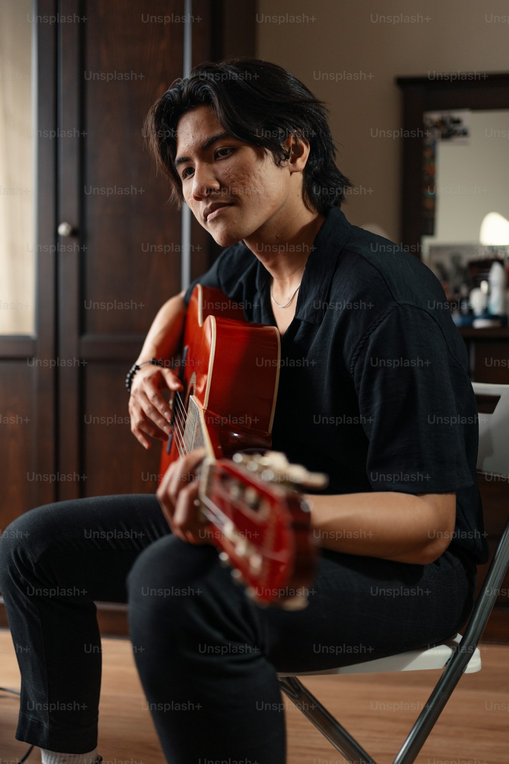 um homem sentado em uma cadeira segurando uma guitarra vermelha