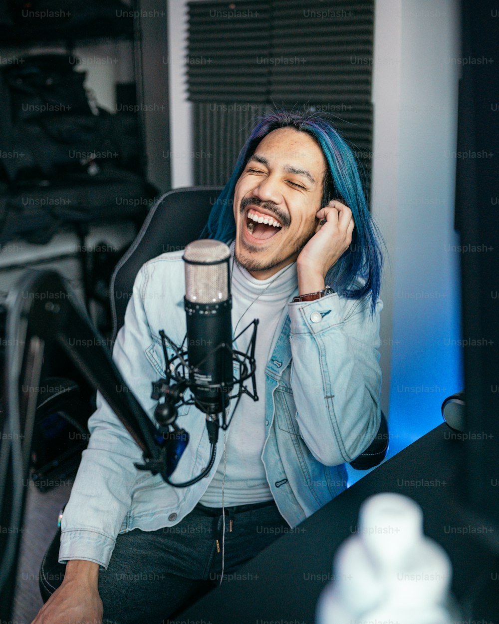 a man with blue hair sitting in front of a microphone
