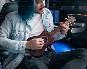 Un hombre con cabello azul tocando un ukelele