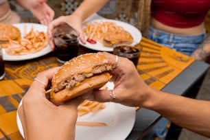 a person holding a hamburger in front of a plate of food