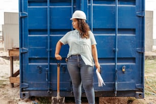 a woman standing in front of a blue container holding a shovel