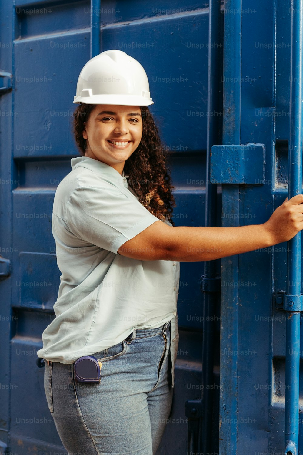 a woman wearing a white hard hat leaning against a blue wall