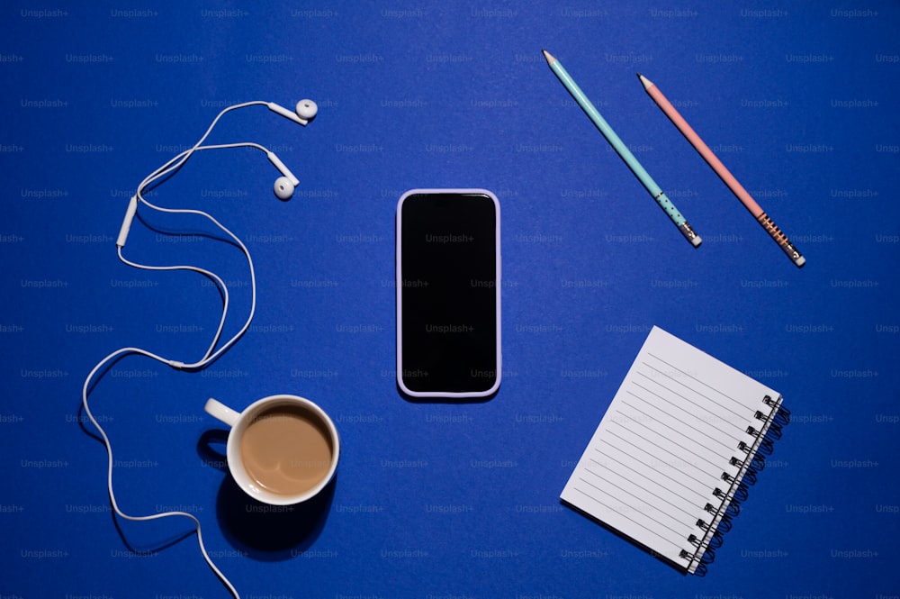 una taza de café, auriculares, un bloc de notas y un teléfono celular