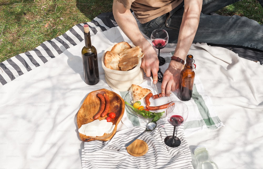 a person sitting on a blanket with food and wine
