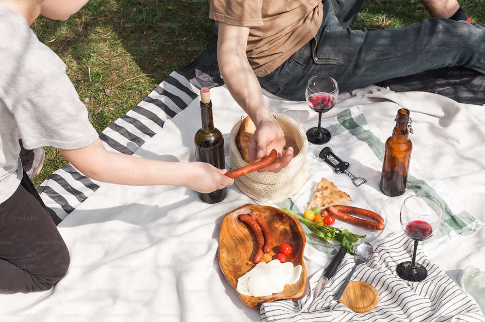 two people sitting on a blanket with food and wine