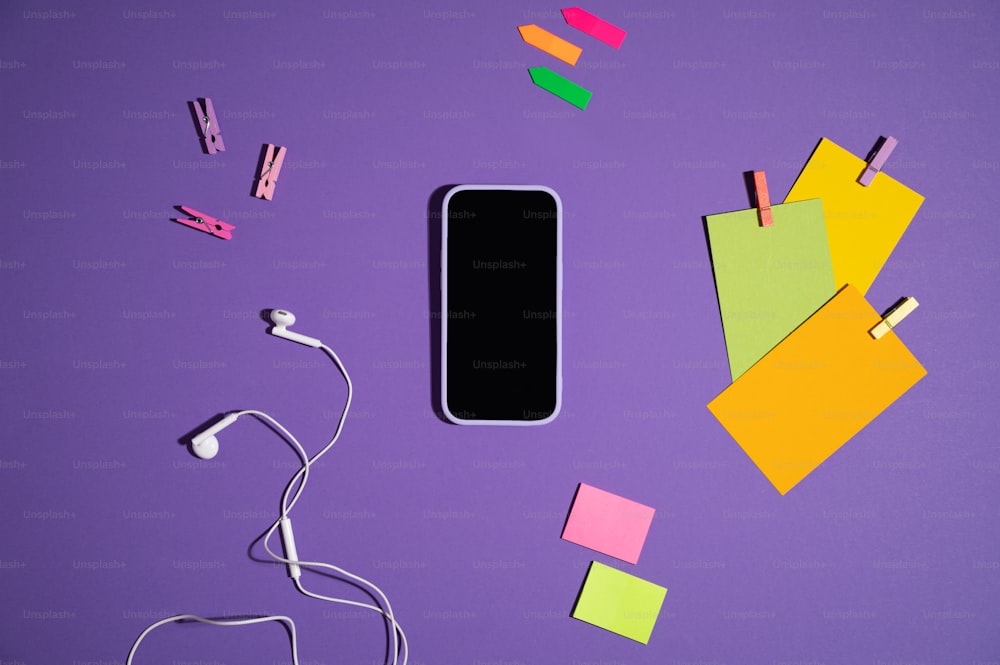 un teléfono celular, auriculares y notas adhesivas sobre un fondo púrpura