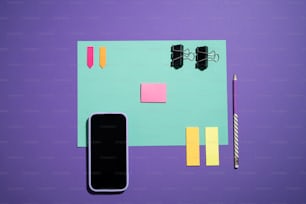 um telefone celular, caneta e notas adesivas em um fundo roxo