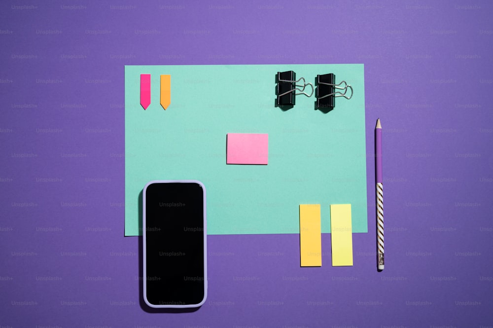 um telefone celular, caneta e notas adesivas em um fundo roxo