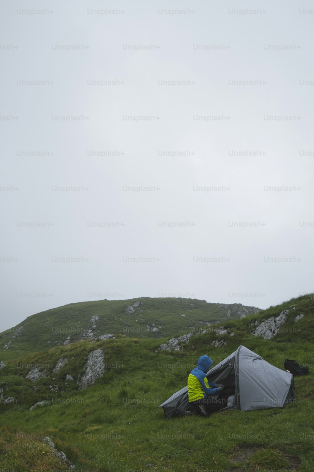 Un hombre sentado en una tienda de campaña en la cima de una exuberante ladera verde