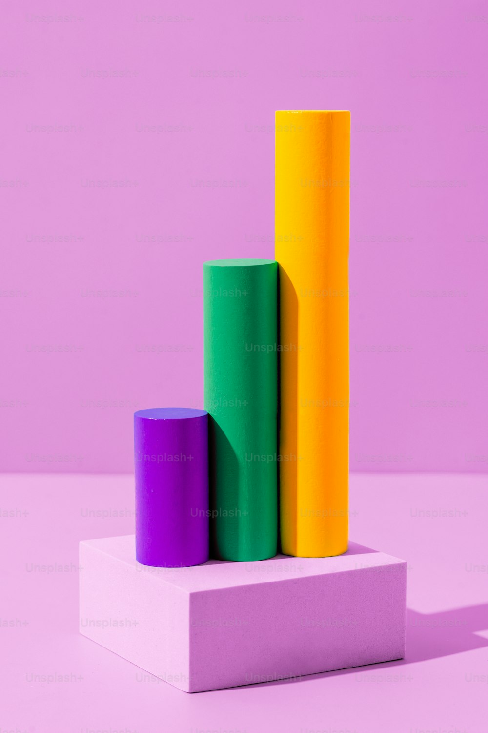 a stack of three different colored cylinders on a pink surface