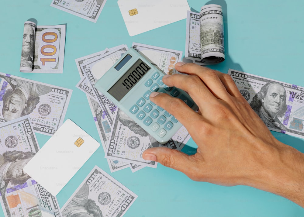 uma pessoa segurando uma calculadora na frente de uma pilha de dinheiro