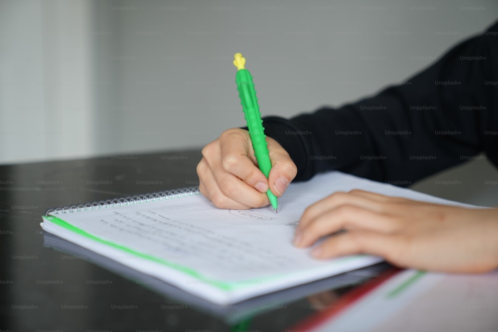 une personne écrivant sur un cahier avec un stylo vert
