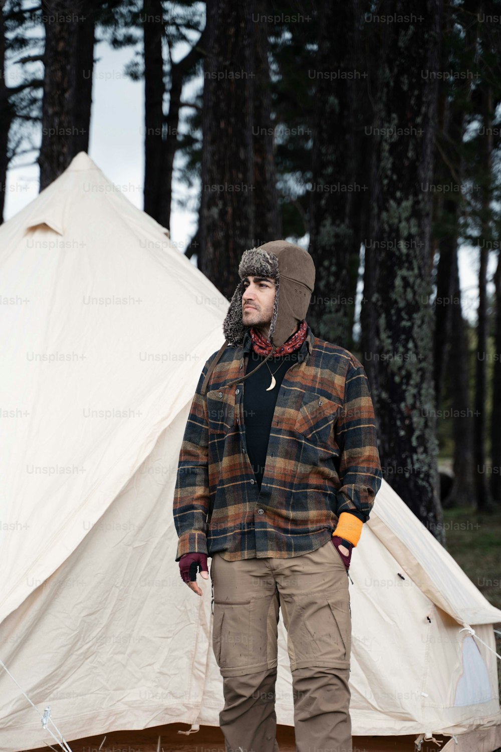 a man standing next to a tent in the woods