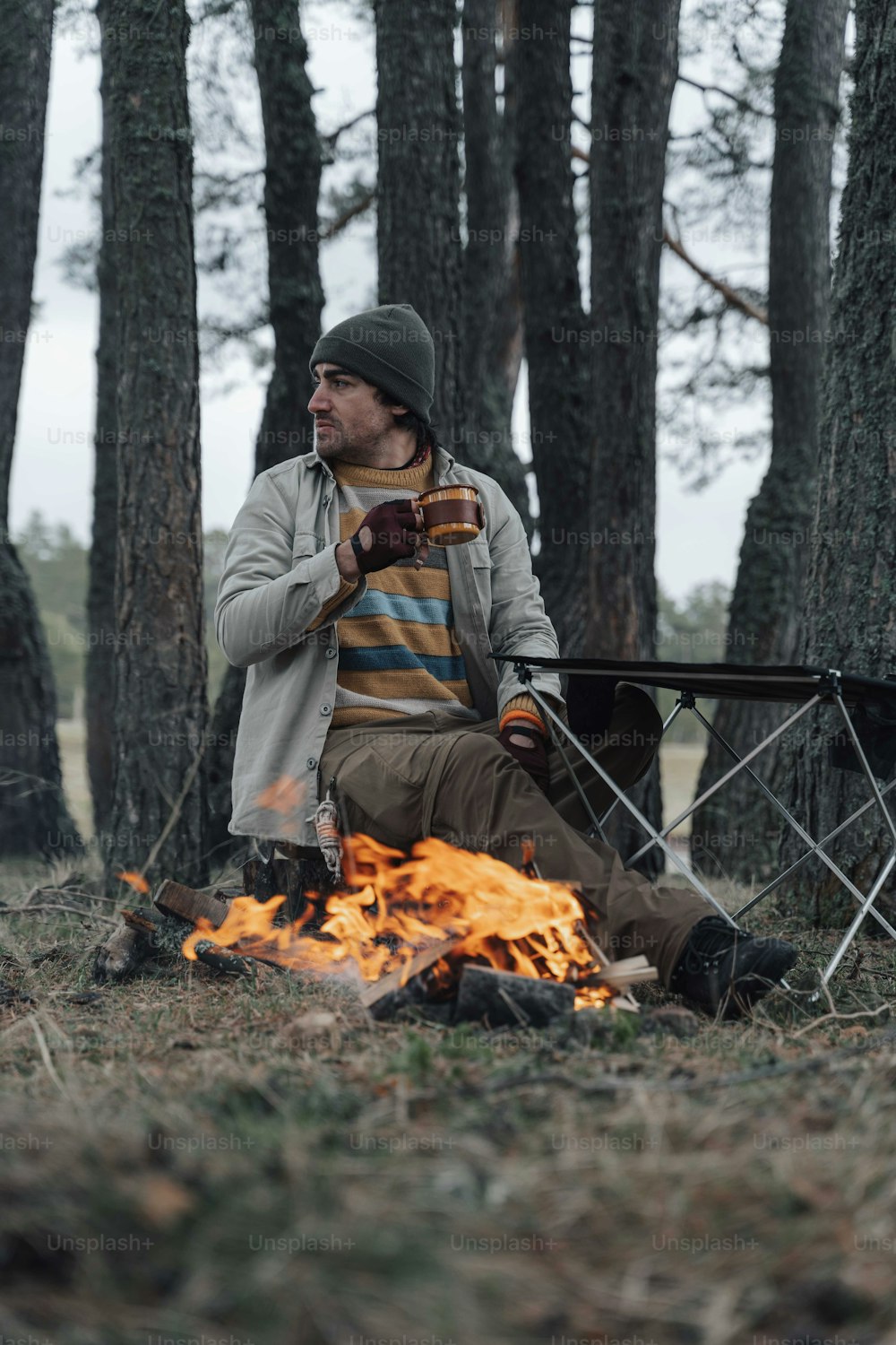 a man sitting next to a fire in a forest