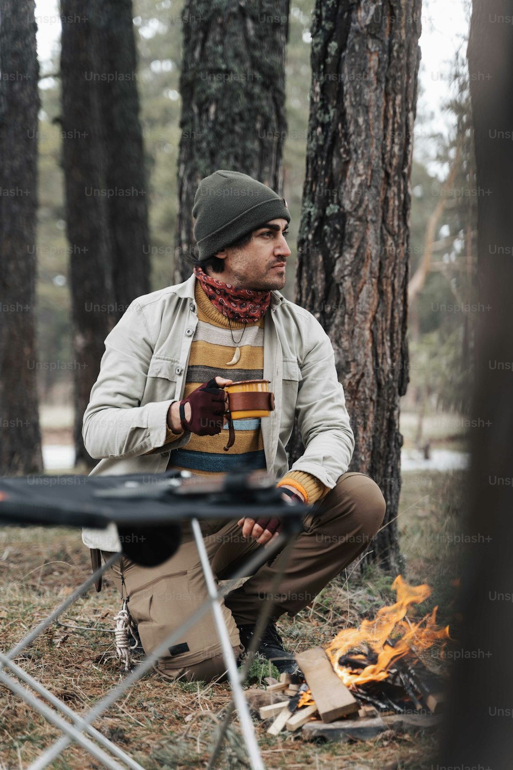 a man sitting next to a campfire in the woods
